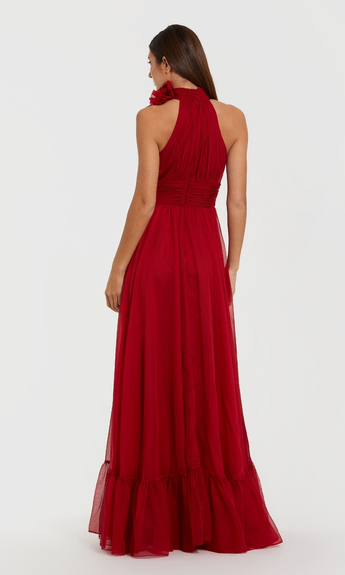 A woman faces away, modeling the Mac Duggal 56254 long formal dress in dark red chiffon with a halter neckline and ruffled hem, standing against a plain white background.